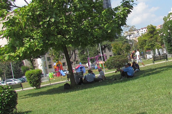 people rest in shade and children play in park