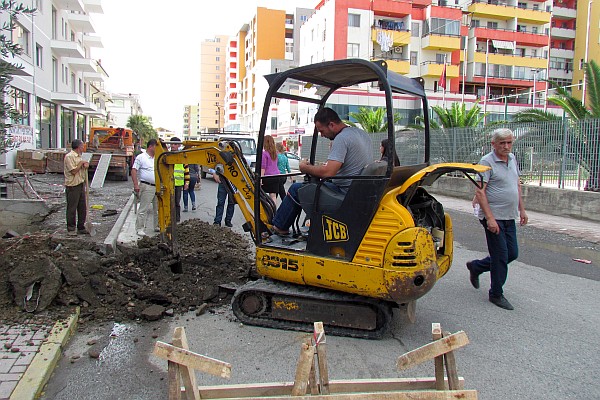 a small excavqator is digging a ditch across a street