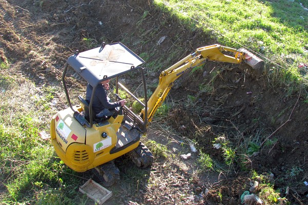 a small excavator works to smooth out the banks of the Drini