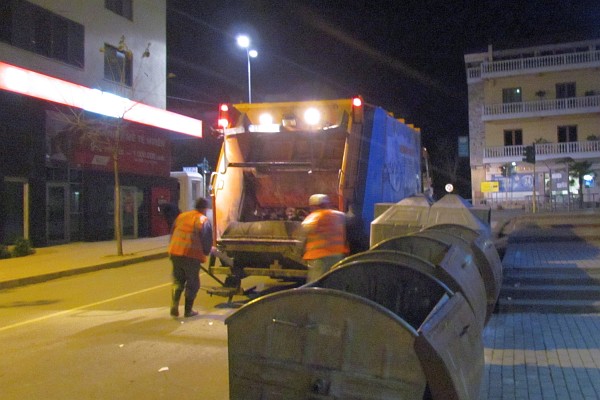 a garbage truck empties the garbage bins along the street