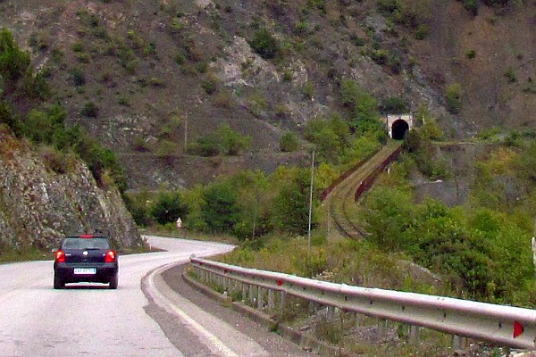 road goes down and around; tracks are on the level through a tunnel